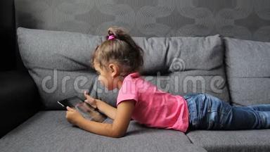 小女孩躺在沙发上用平板电脑。 小女孩躺着玩平板电脑